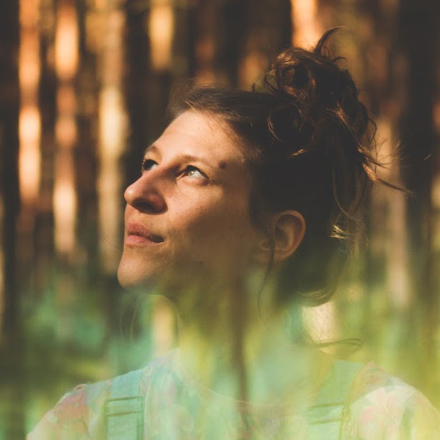 Artist Laura Weider in the forest with some iriedescent effects, she is looking up into the skies between trees